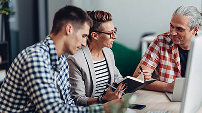 Can Employers Require Employees To Get Vaccinated? A woman and two men, dressed casually, sitting at a table while having a discussion